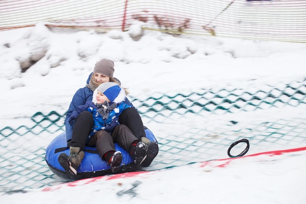 Familia divirtiéndose en el tubo de nieve, la madre con un niño está montando un tubo
