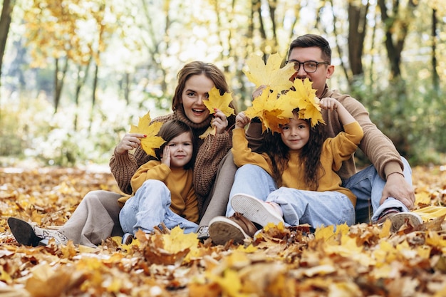 Foto familia con dos hijas sentadas en el parque en hojas de otoño