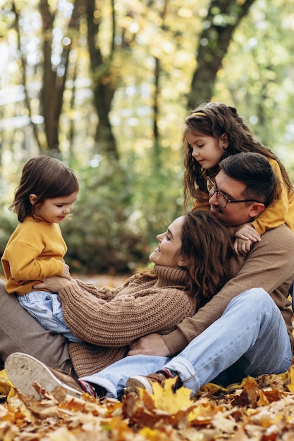 Familia con dos hijas sentadas en el parque en hojas de otoño