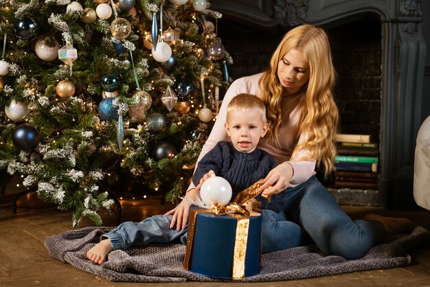 Una familia de dos madre e hijo desempacando un regalo cerca del árbol de navidad el concepto de una fiesta navideña ...