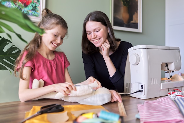 Familia, dos niñas hermanas adolescente y menor juntos coser conejito de muñeca de juguete. Pasatiempos, ocio, creatividad y habilidades adolescentes.