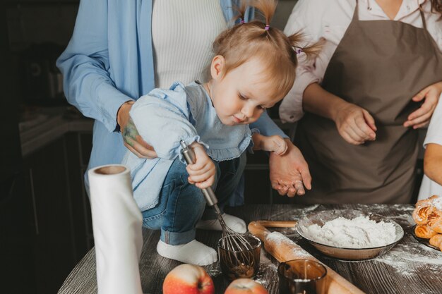 Família: duas mulheres e crianças preparam um bolo de aniversário na cozinha.