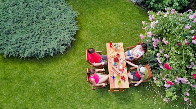 Família e amigos comendo juntos ao ar livre na festa de verão no jardim. Vista aérea da mesa com alimentos e bebidas de cima. Conceito de lazer, férias e piquenique