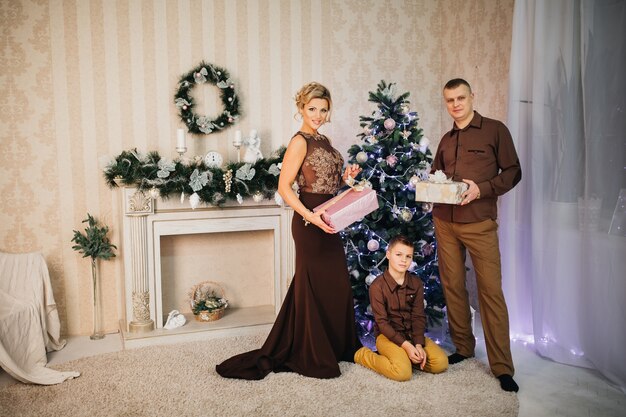 Família e filho posam perto da árvore de Natal com presentes nas mãos