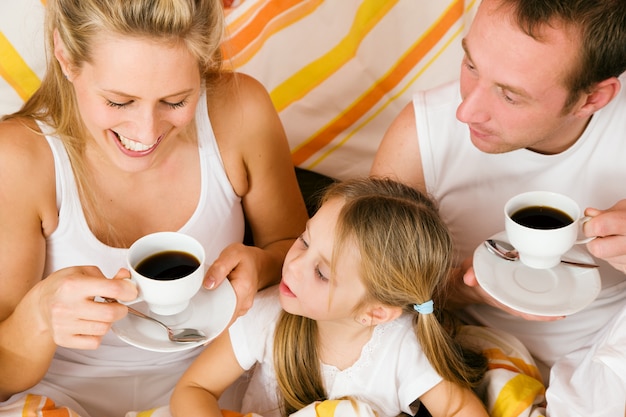 Família e gato tomando café da manhã na cama