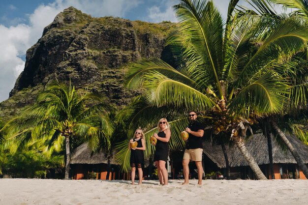 Una familia elegante vestida de negro con cocos en las manos en la playa de la isla de MauricioHermosa familia en la isla de Mauricio en el océano Índico