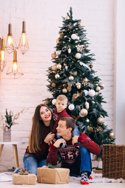 Família em lindos suéteres sentada perto de uma árvore de Natal.