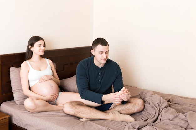 Familia embarazada feliz Marido masajeando las piernas de su esposa embarazada y sentados juntos en el sofá de su casa