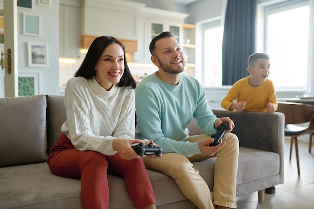 Familia encantada con niño. Hijo feliz viendo mientras madre y padre juegan videojuegos