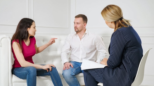 Familia enfrenta dificultades en las relaciones. Pareja joven visitando la oficina del terapeuta matrimonial profesional, peleando entre sí en la sesión de terapia.