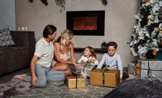 La familia está celebrando la Navidad en casa, mamá, papá y niños felices abriendo regalos de año nuevo