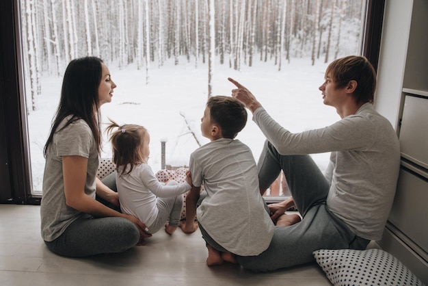 La familia está sentada en la ventana y mirando el bosque de invierno. Buen espíritu de año nuevo. Mañana en pijama.