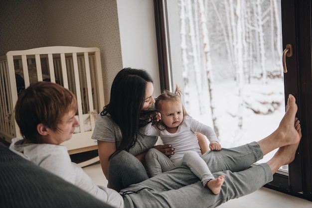 La familia está sentada en la ventana y mirando el bosque de invierno. Buen espíritu de año nuevo. Mañana en pijama.