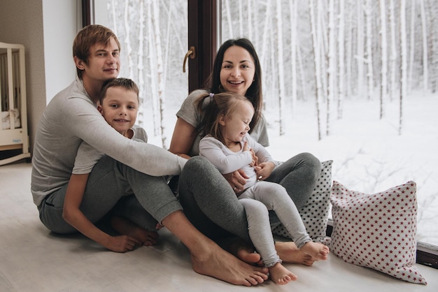 La familia está sentada en la ventana y mirando el bosque de invierno. Buen espíritu de año nuevo. Mañana en pijama.