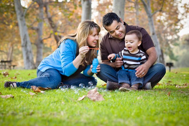 Família étnica de raça mista feliz brincando com bolhas no parque