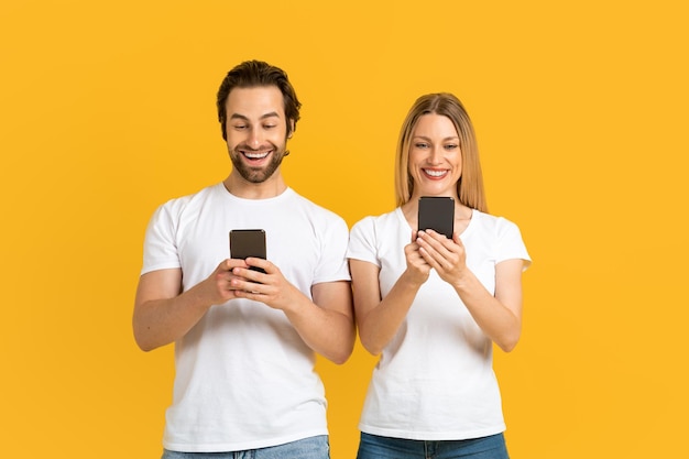 Familia europea joven sonriente en camisetas blancas escribiendo en teléfonos chateando en las redes sociales