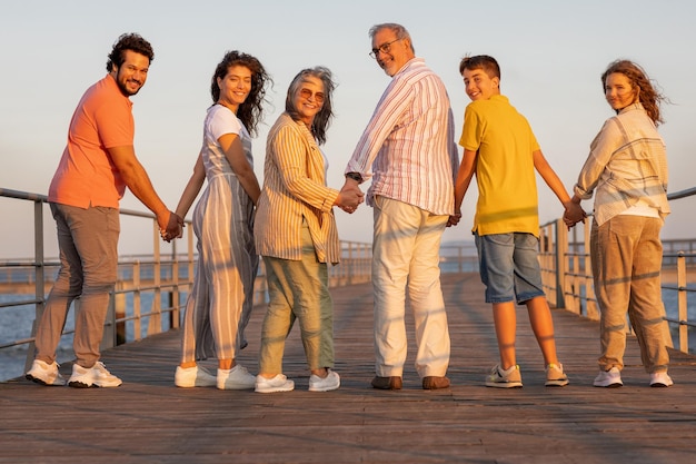 Família europeia feliz de várias gerações, de mãos dadas, a desfrutar de férias na praia, a divertir-se ao ar livre.