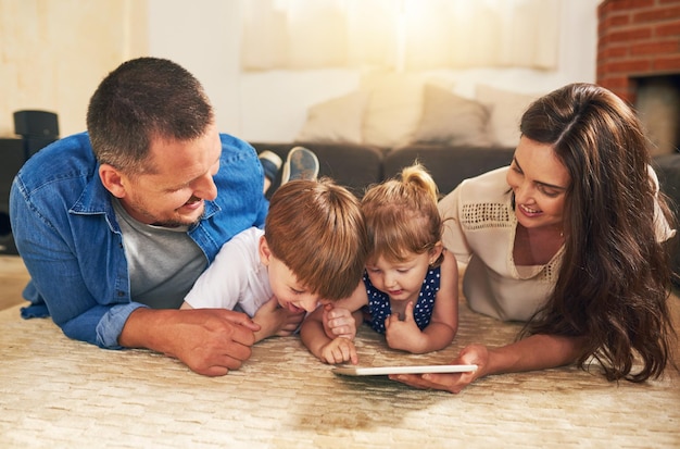 La familia experta en tecnología está más conectada que nunca Foto de un adorable hermano y hermana usando una tableta digital con sus padres en el piso de su casa