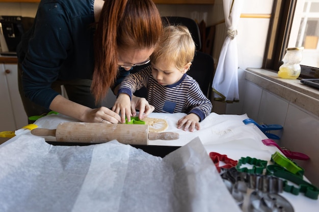 Família fazendo biscoitos uma mulher com seu filho pequeno cortando dinossauros de massa crua com um molde