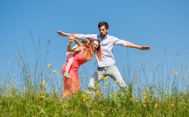 Família fazendo o avião em um prado de verão sob um céu azul claro