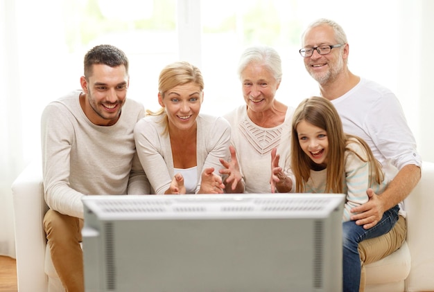 Família, felicidade, geração e conceito de pessoas - família feliz sentada no sofá e assistindo tv em casa