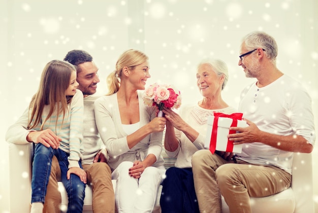 família, felicidade, geração, feriados e conceito de pessoas - família feliz com um monte de flores e caixa de presente sentado no sofá em casa