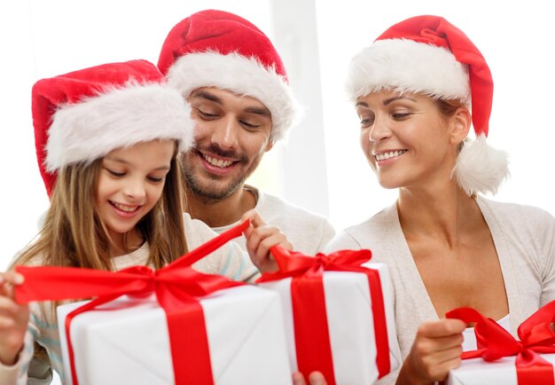 família, felicidade, geração, feriados e conceito de pessoas - família feliz em chapéus de ajudante de papai noel com caixas de presente sentado no sofá em casa