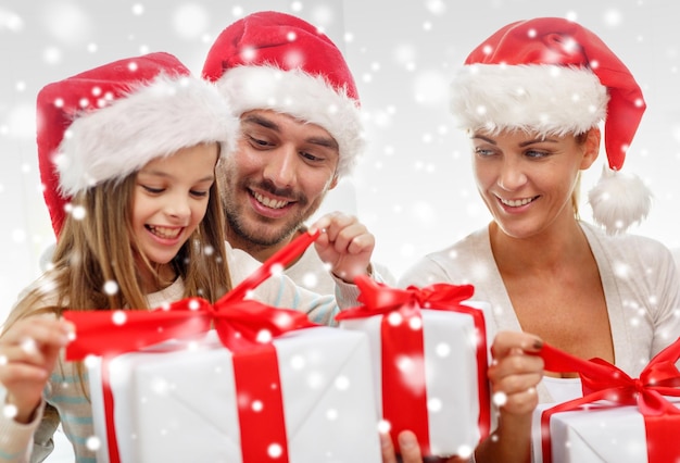 família, felicidade, geração, feriados e conceito de pessoas - família feliz em chapéus de ajudante de papai noel com caixas de presente sentado no sofá em casa