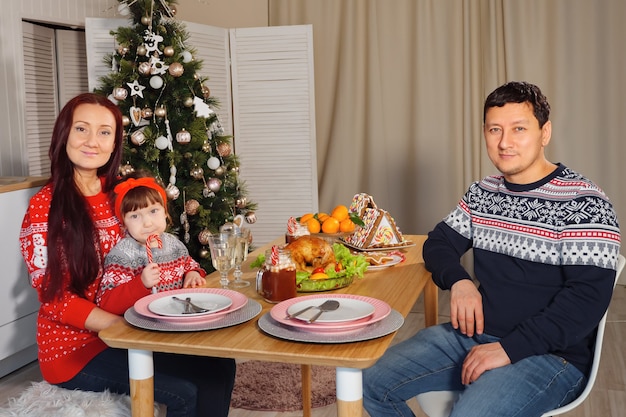 Família feliz à mesa no fundo de uma árvore de natal decorada