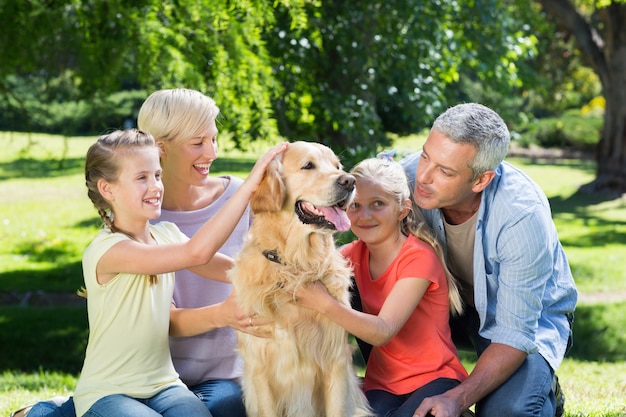 Foto família feliz acariciando seu cachorro no parque