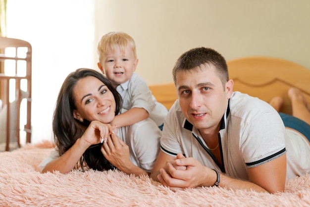 Familia feliz acostada en la cama y abrazando a mamá papá y a su pequeño hijo