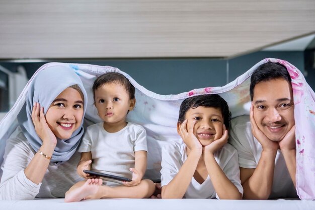 Familia feliz acostada en la cama bajo una manta