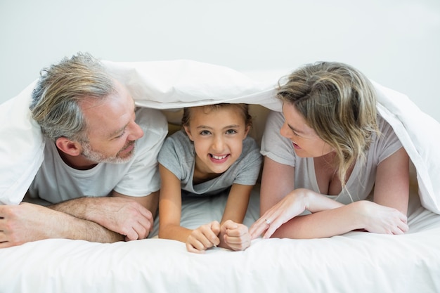 Familia feliz acostado bajo una manta en la cama en casa