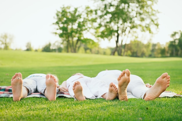 Familia feliz acostado sobre la hierba verde en el parque. Relajación y concepto de estilo de vida saludable