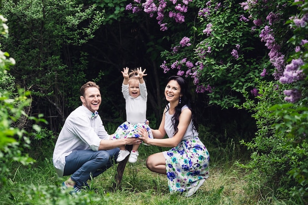 Família feliz alegre abraçando perto de arbustos de flor lilás.