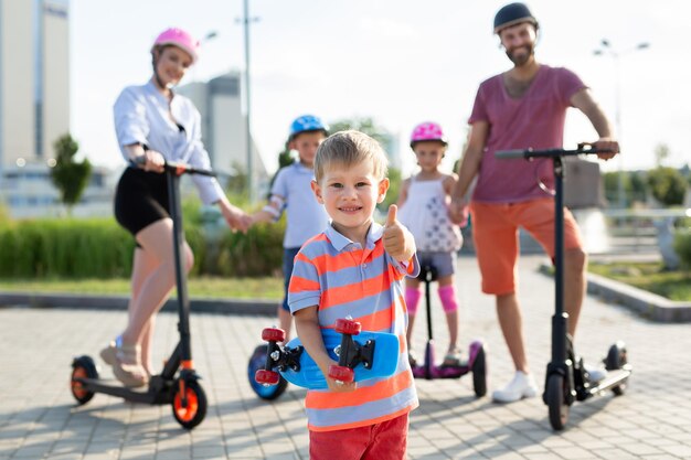 Família feliz andando de scooters elétricos e giroscópios no parque em primeiro plano um menino