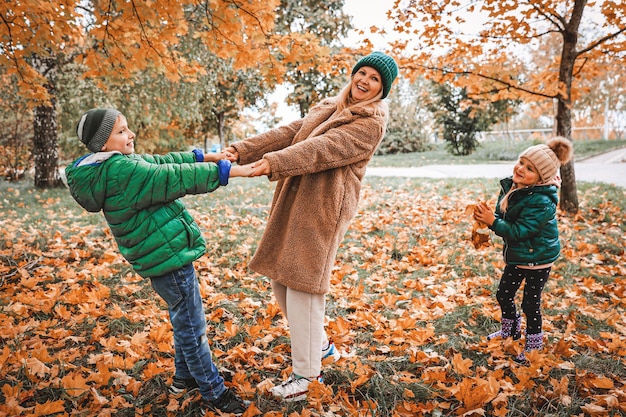 Família feliz andando no parque ensolarado e joga laranja maple deixa mãe com crianças aproveitando o clima de outono ao ar livre