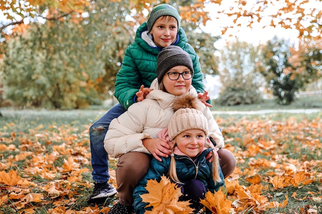 Família feliz andando no parque ensolarado e joga laranja maple deixa mãe com crianças aproveitando o clima de outono ao ar livre