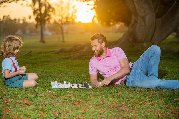 Família feliz ao ar livre pai e filho jogando xadrez no jardim de verão garotinho joga xadrez com os pais