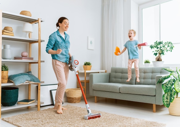 Familia feliz aspirando la habitación. Madre e hija haciendo la limpieza en la casa.