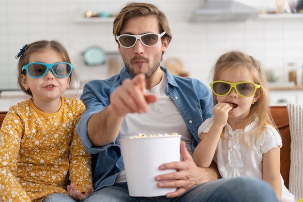 Família feliz assistindo tv em casa e comendo pipoca.