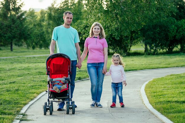 Família feliz ativa andando no parque de verão com um carrinho com a filha