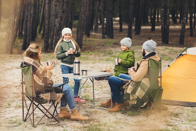 Família feliz bebendo chá quente durante a viagem de acampamento