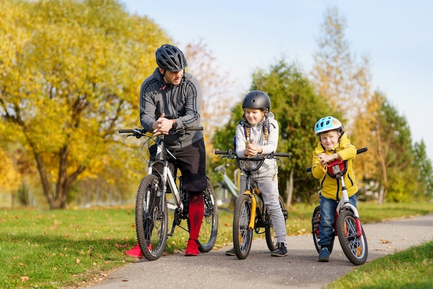 Familia feliz con bicicletas al aire libre mirando a la cámara y sonriendo mientras camina en una fila con bicicletas