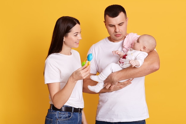 Família feliz brincando com sua filha recém-nascida enquanto posa isolada na parede amarela