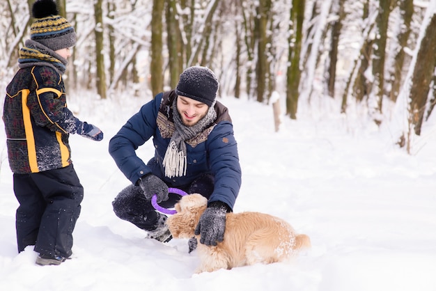 Família feliz, brincando com um cachorro na neve ao ar livre