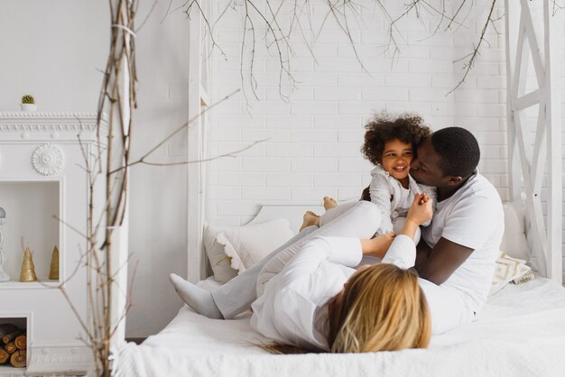 Família feliz brincando na cama com a filha