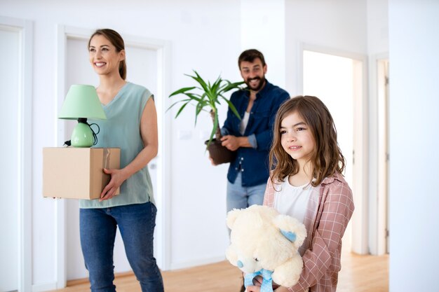 Familia feliz con cajas de cartón, flores y juguetes en su nueva casa inmobiliaria.