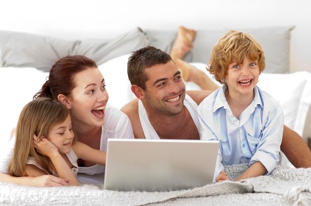 Familia feliz en la cama usando una computadora portátil