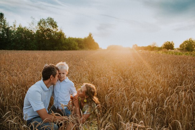 una familia feliz camina por un campo de trigo divirtiéndose y riendo al atardecer